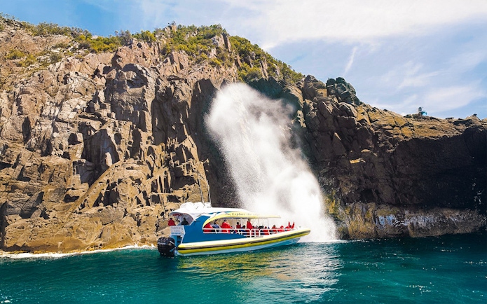 Cruise boat near rocky cliffs and waterfall on Bruny Island Wilderness Cruise.