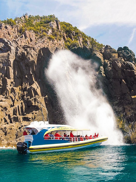 Cruise boat near rocky cliffs and waterfall on Bruny Island Wilderness Cruise.