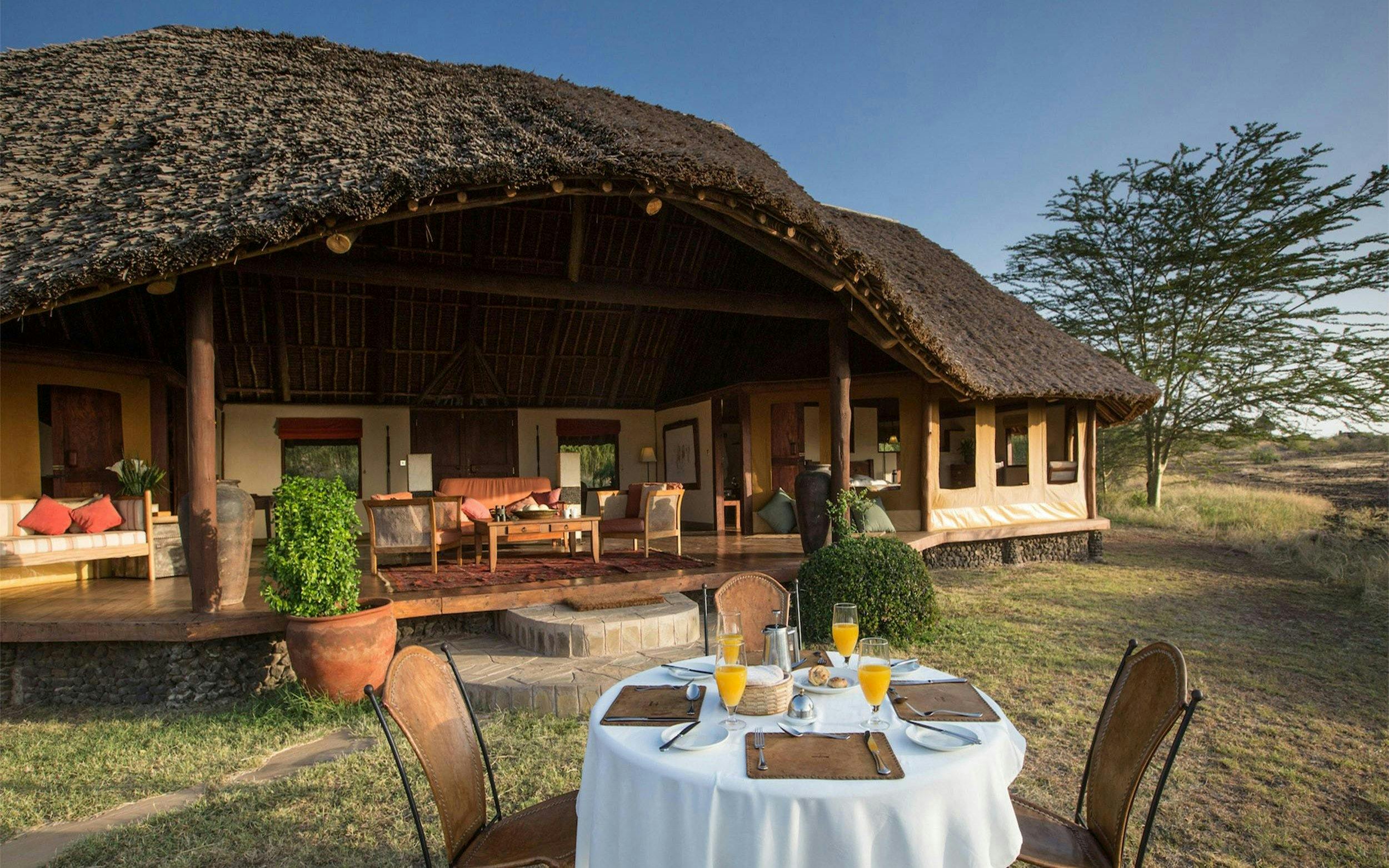 Outdoor dining setup at a lodge in Amboseli & Tsavo Safari, featuring a thatched-roof veranda.