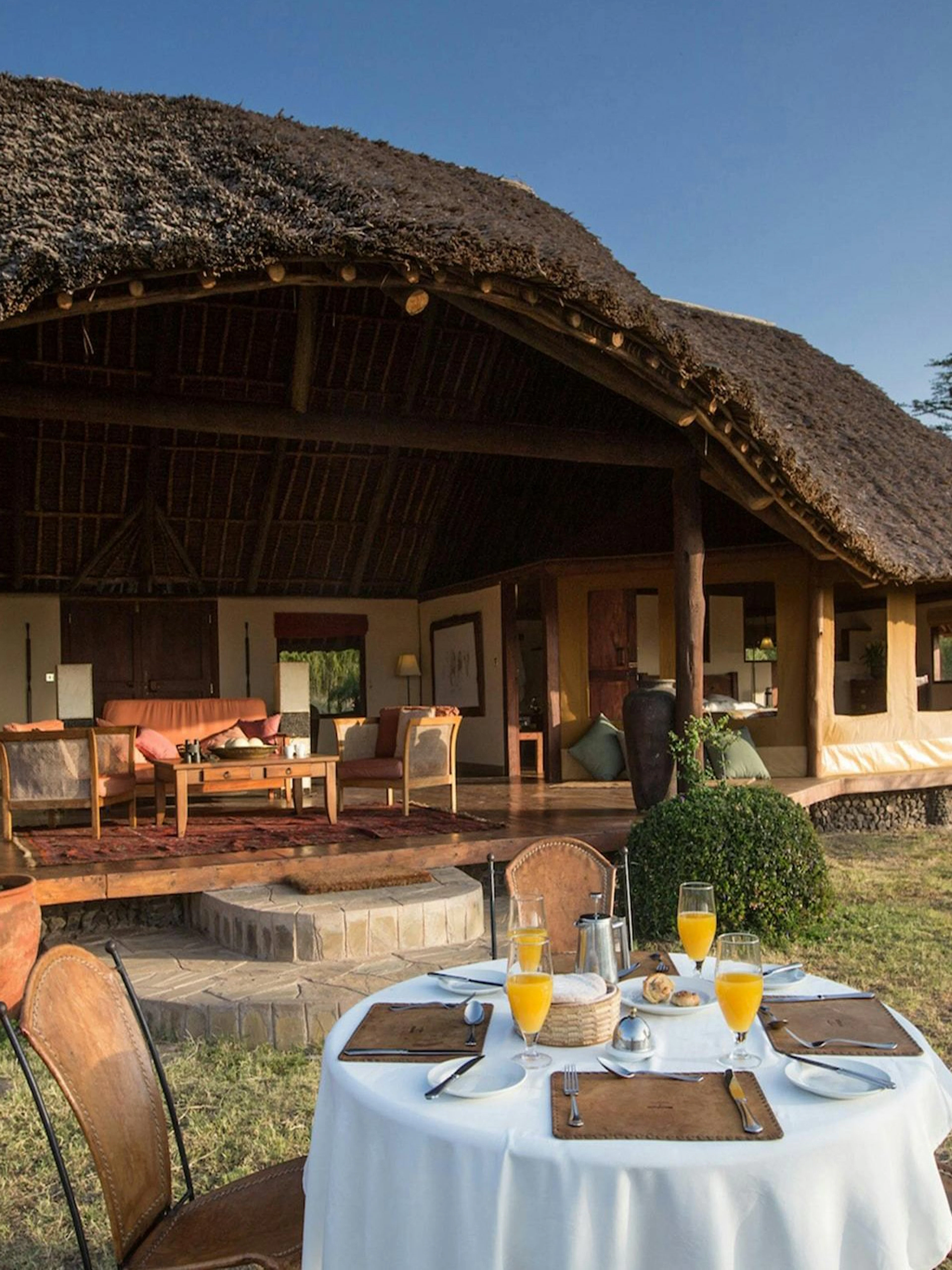 Outdoor dining setup at a lodge in Amboseli & Tsavo Safari, featuring a thatched-roof veranda.
