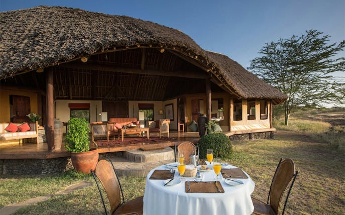 Outdoor dining setup at a lodge in Amboseli & Tsavo Safari, featuring a thatched-roof veranda.