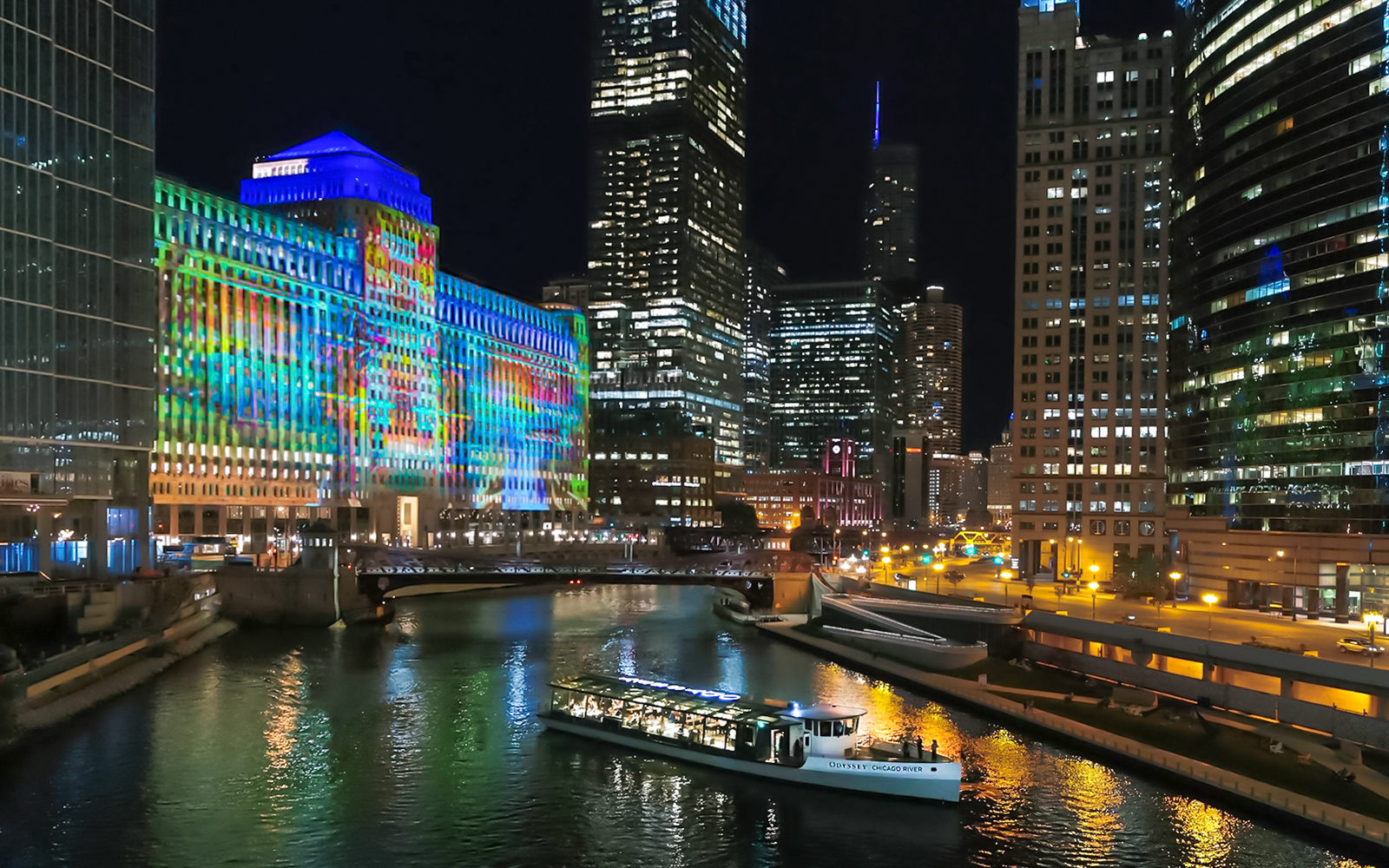 Chicago River at night with a boat, illuminated skyscrapers, and the Merchandise Mart building.