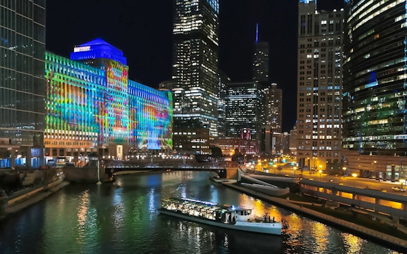 Chicago River at night with a boat, illuminated skyscrapers, and the Merchandise Mart building.