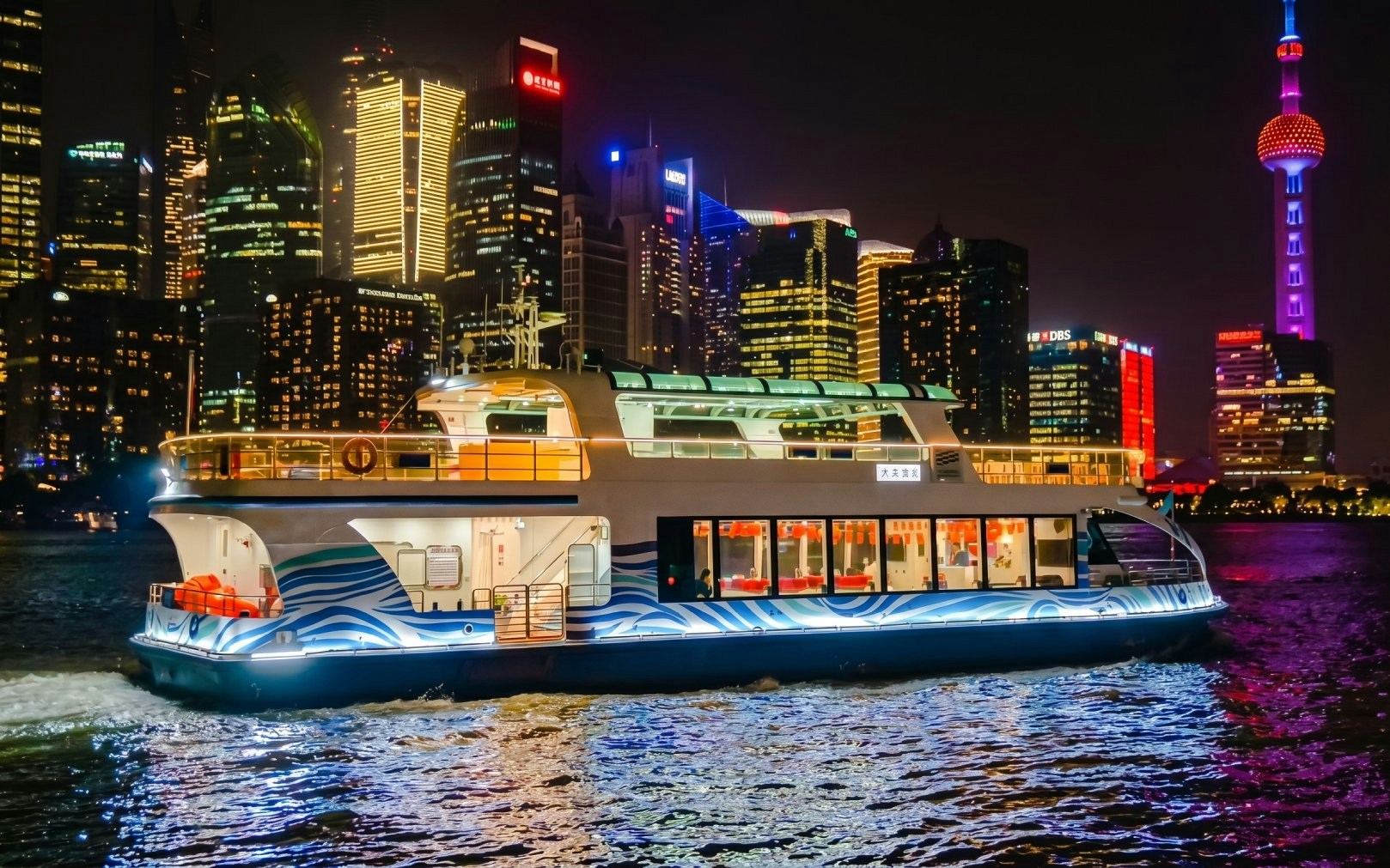Cruise boat on Huangpu River with Shanghai skyline at night.