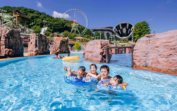 Family enjoying a pool at Tokyo Summerland with water slides and Ferris wheel in the background.
