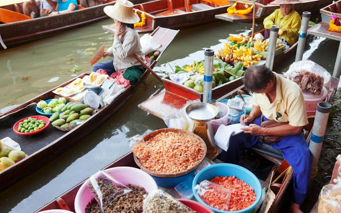 Vendors selling fruits and goods at Damnoen Saduak Floating Market, Thailand.