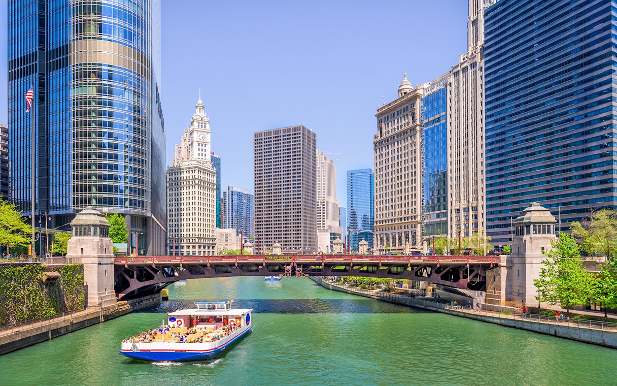 Chicago River cruise boat passing iconic skyscrapers and bridges.