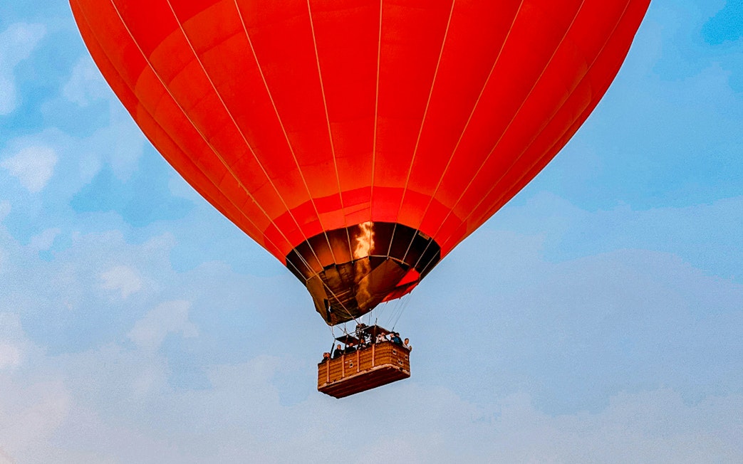 Hot air balloon flying over Luxor with passengers in the basket.