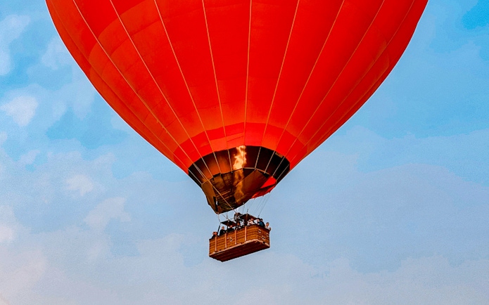 Hot air balloon flying over Luxor with passengers in the basket.