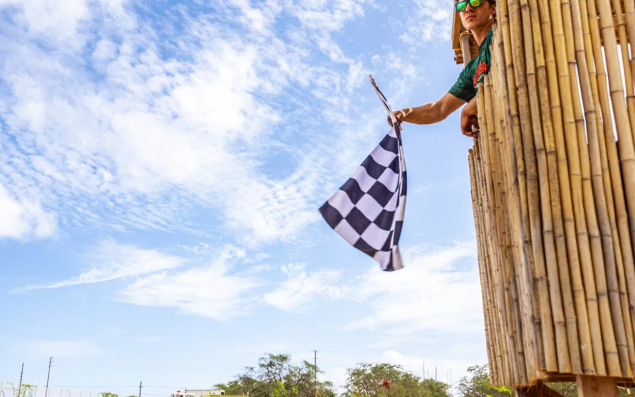 Person waving checkered flag from bamboo tower during Oahu electric dirt bike experience.