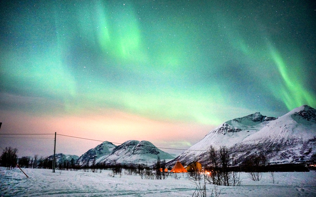 Northern Lights over snowy mountains in Tromso during reindeer sledding tour.