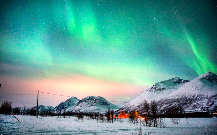 Northern Lights over snowy mountains in Tromso during reindeer sledding tour.