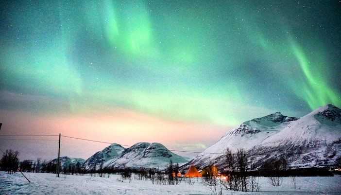 Northern Lights over snowy mountains in Tromso during reindeer sledding tour.