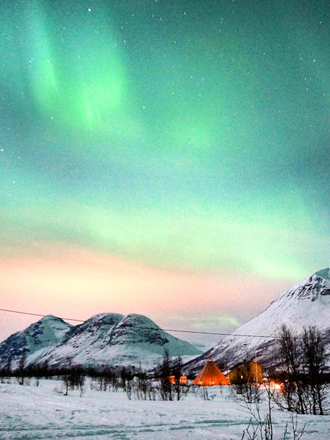 Northern Lights over snowy mountains in Tromso during reindeer sledding tour.