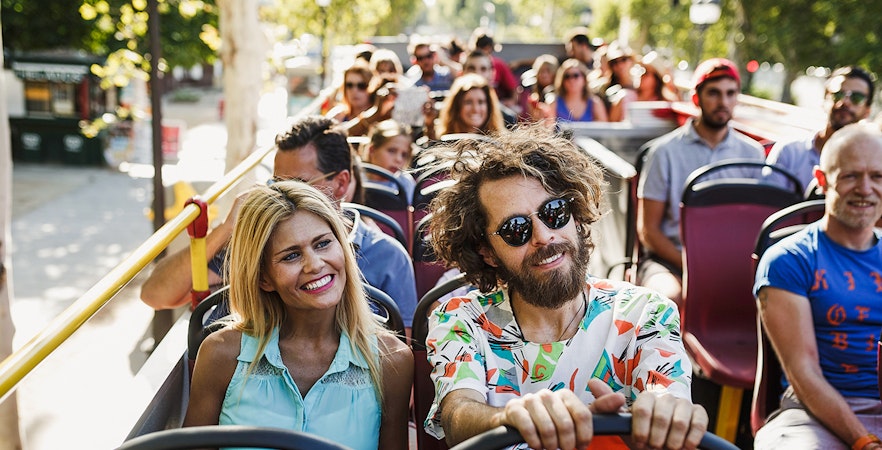 Tourists enjoying a ride on a hop-on hop-off bus in a sunny city.