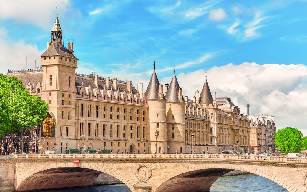 Conciergerie in Paris with historic architecture and Seine River bridge.