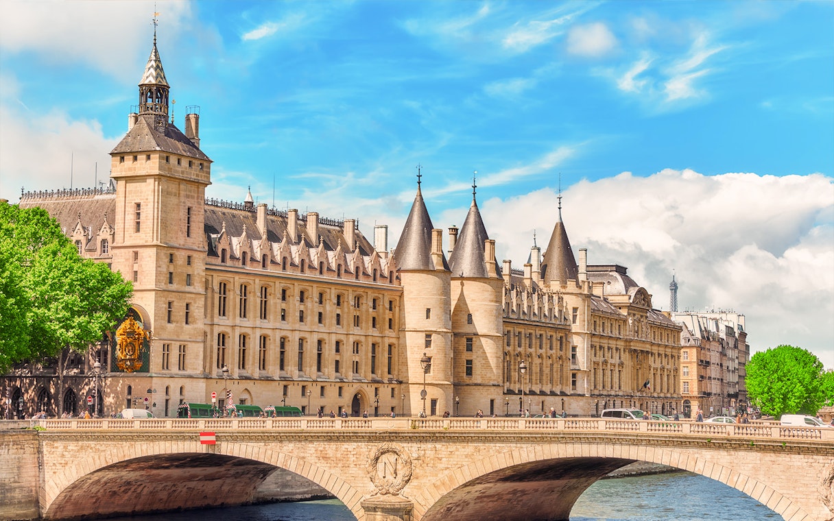 Conciergerie in Paris with historic architecture and Seine River bridge.