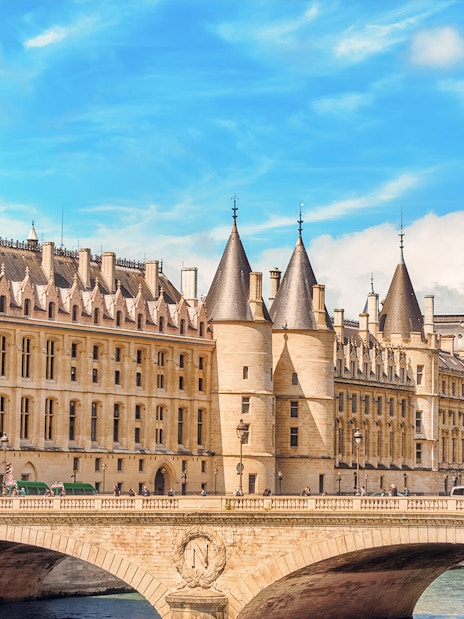 Conciergerie in Paris with historic architecture and Seine River bridge.