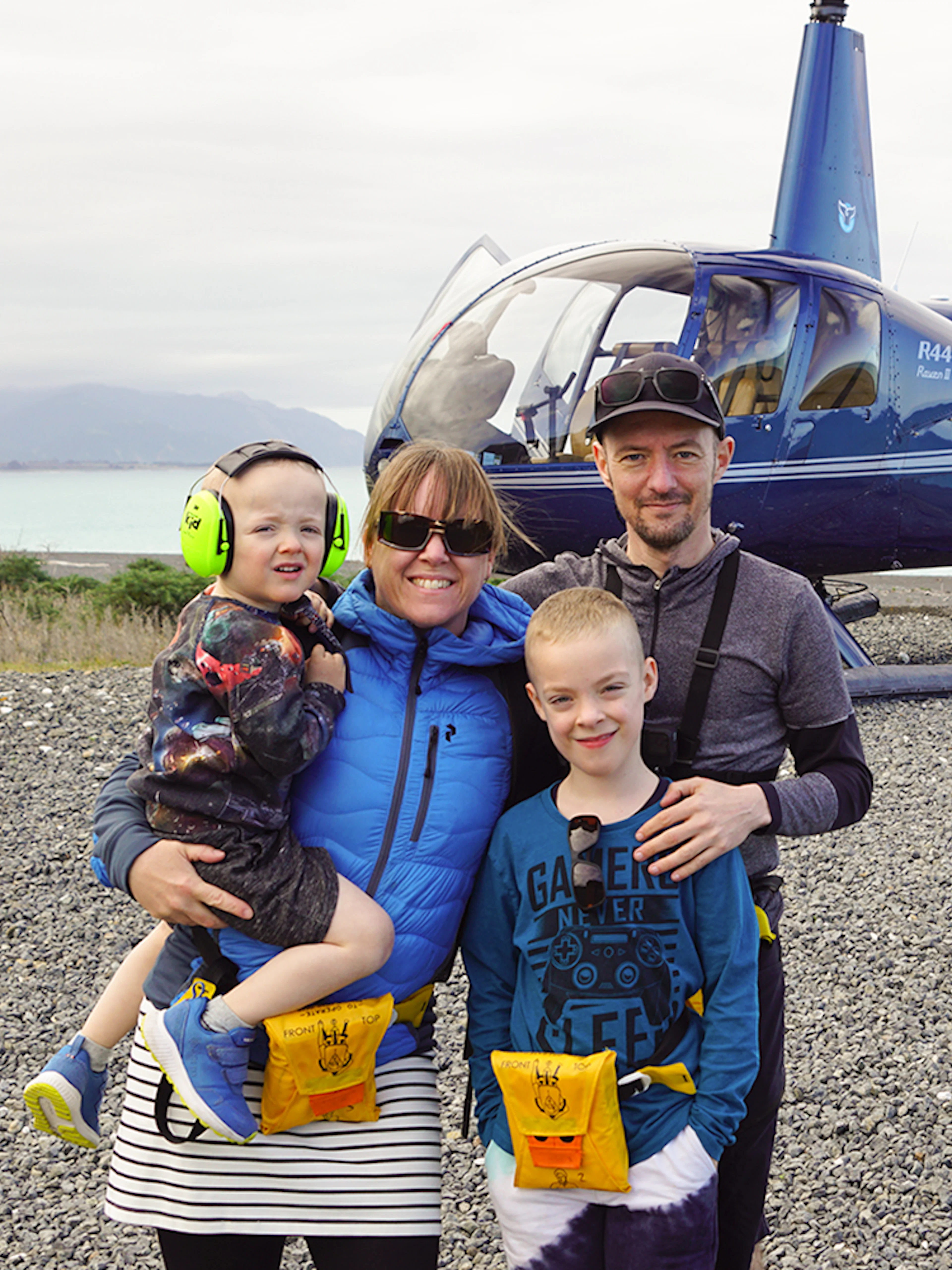 Family posing after helicopter ride in Kaikoura with ocean and mountains in background.