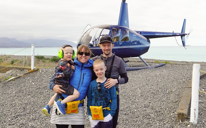 Family posing after helicopter ride in Kaikoura with ocean and mountains in background.