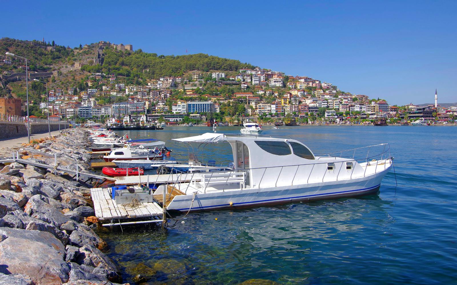 Boat docked along Alanya harbor with hillside view, Turkey.