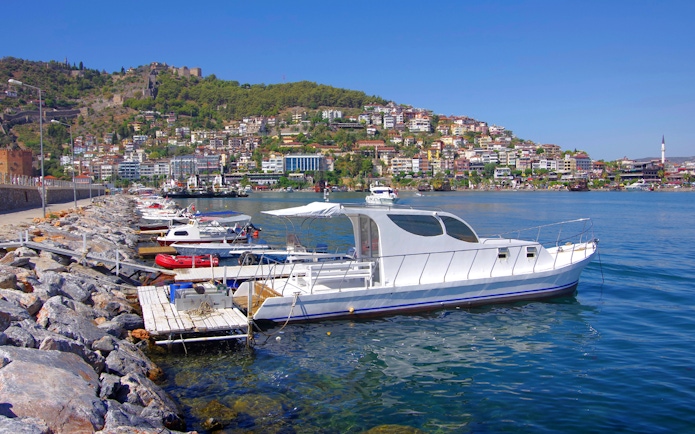 Boat docked along Alanya harbor with hillside view, Turkey.