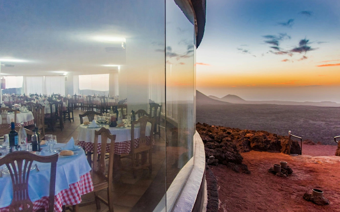 Dining area with set tables overlooking volcanic landscape at sunset, Timanfaya National Park.
