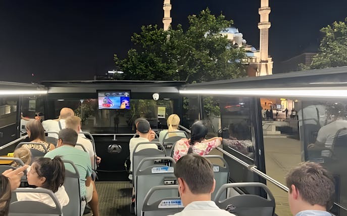 Double-decker bus tour in Istanbul at night with view of illuminated mosque.