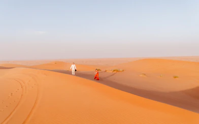 Couple walking on sand dunes in Wahiba Desert during guided tour, Muscat.