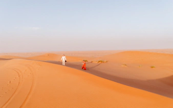 Couple walking on sand dunes in Wahiba Desert during guided tour, Muscat.