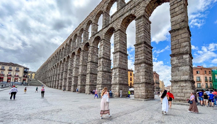 Segovia Aqueduct with tourists walking nearby, Spain.