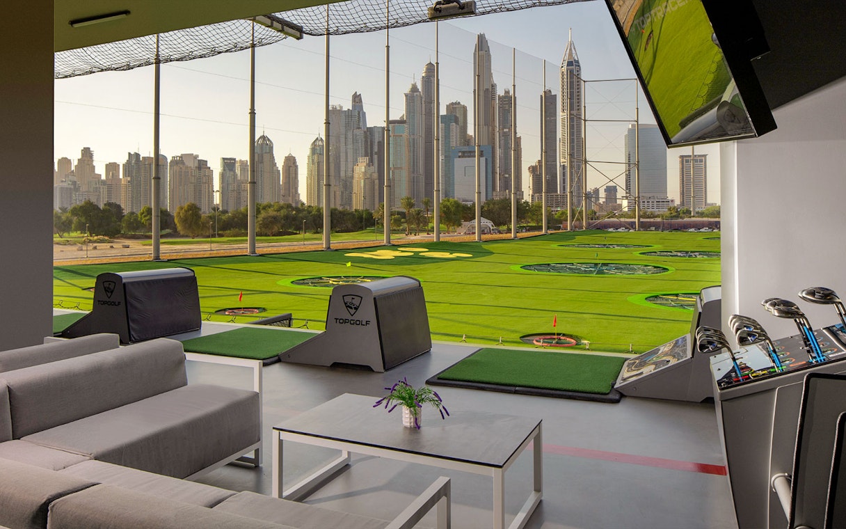 Topgolf Dubai bay with city skyline view and golf equipment.