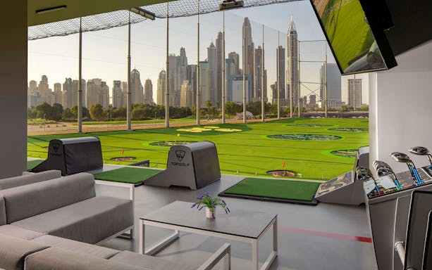 Topgolf Dubai bay with city skyline view and golf equipment.