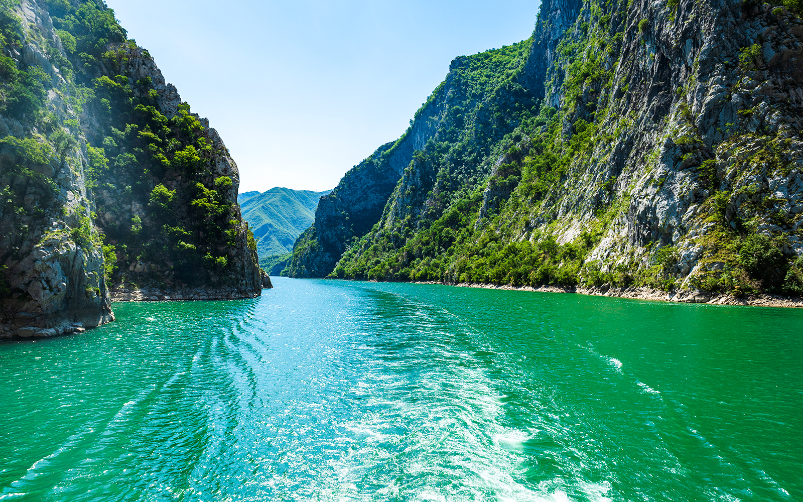 Komani Lake view with surrounding green cliffs during Tirana tour.