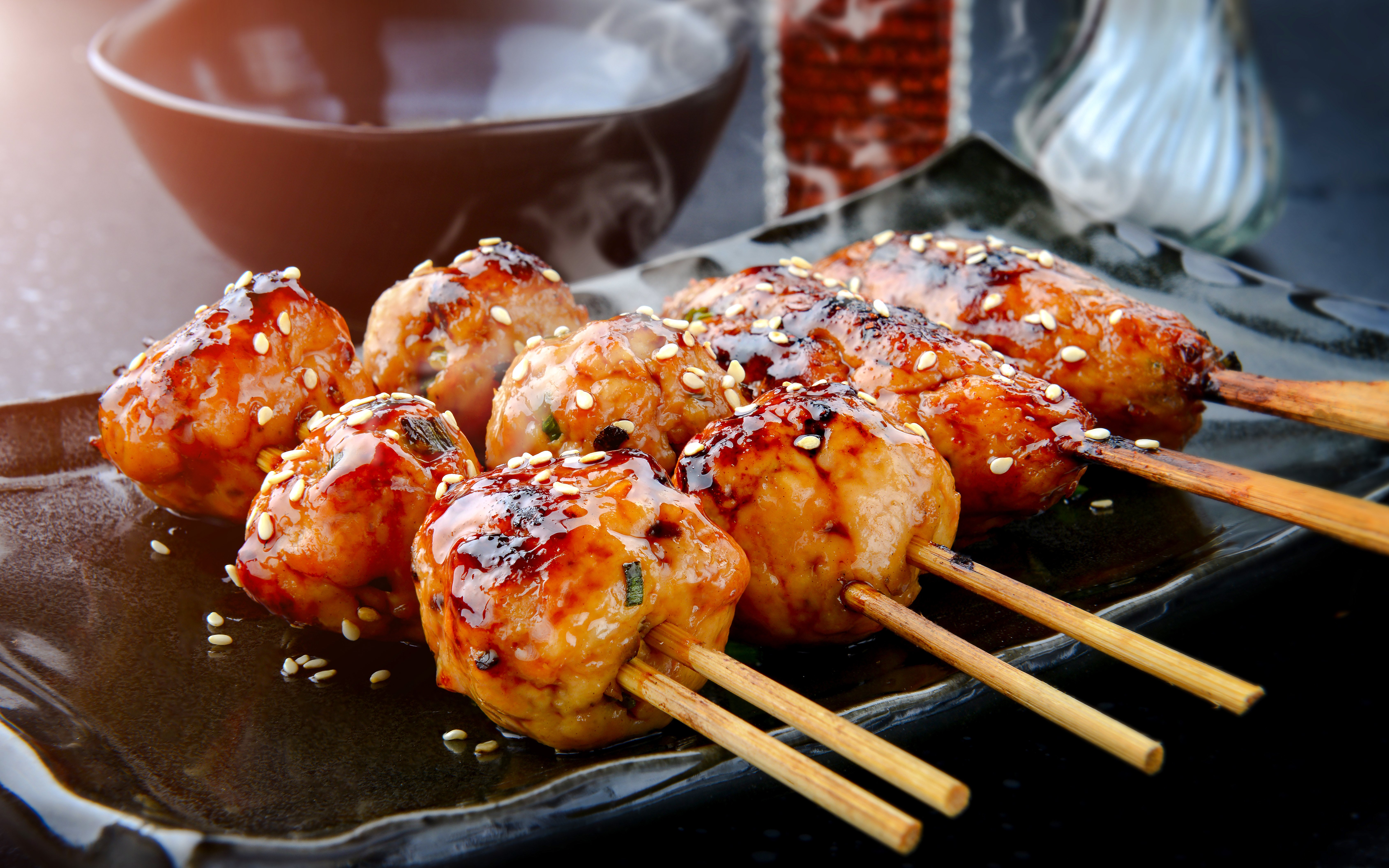 Grilled Japanese tsukune meatballs with sesame seeds on skewers.