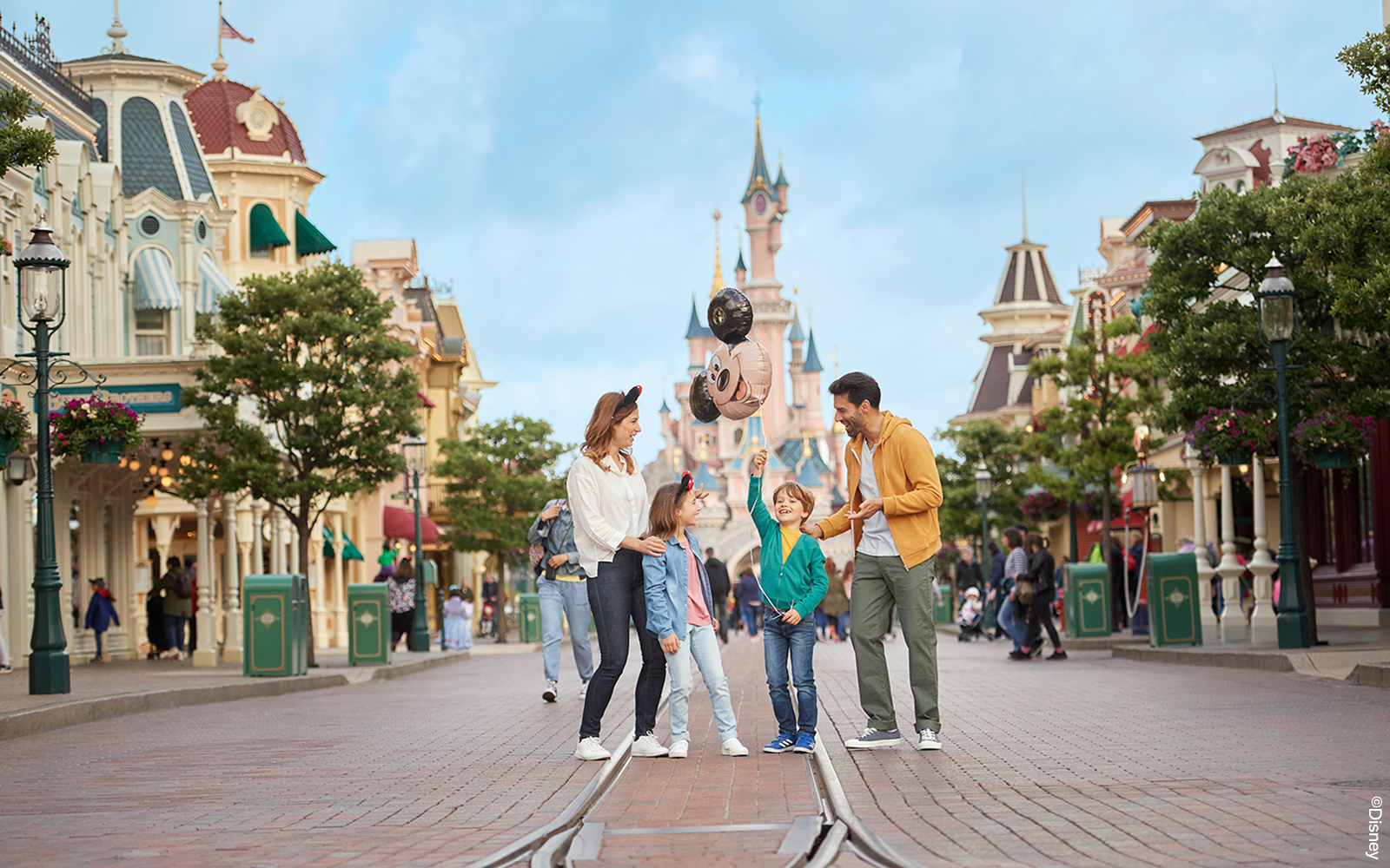 Family enjoying Main Street with Mickey balloons at Disneyland Paris.