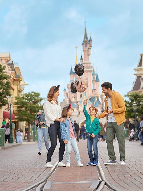 Family enjoying Main Street with Mickey balloons at Disneyland Paris.