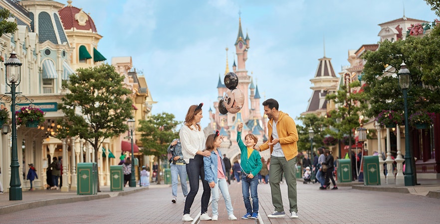 Family enjoying Main Street with Mickey balloons at Disneyland Paris.