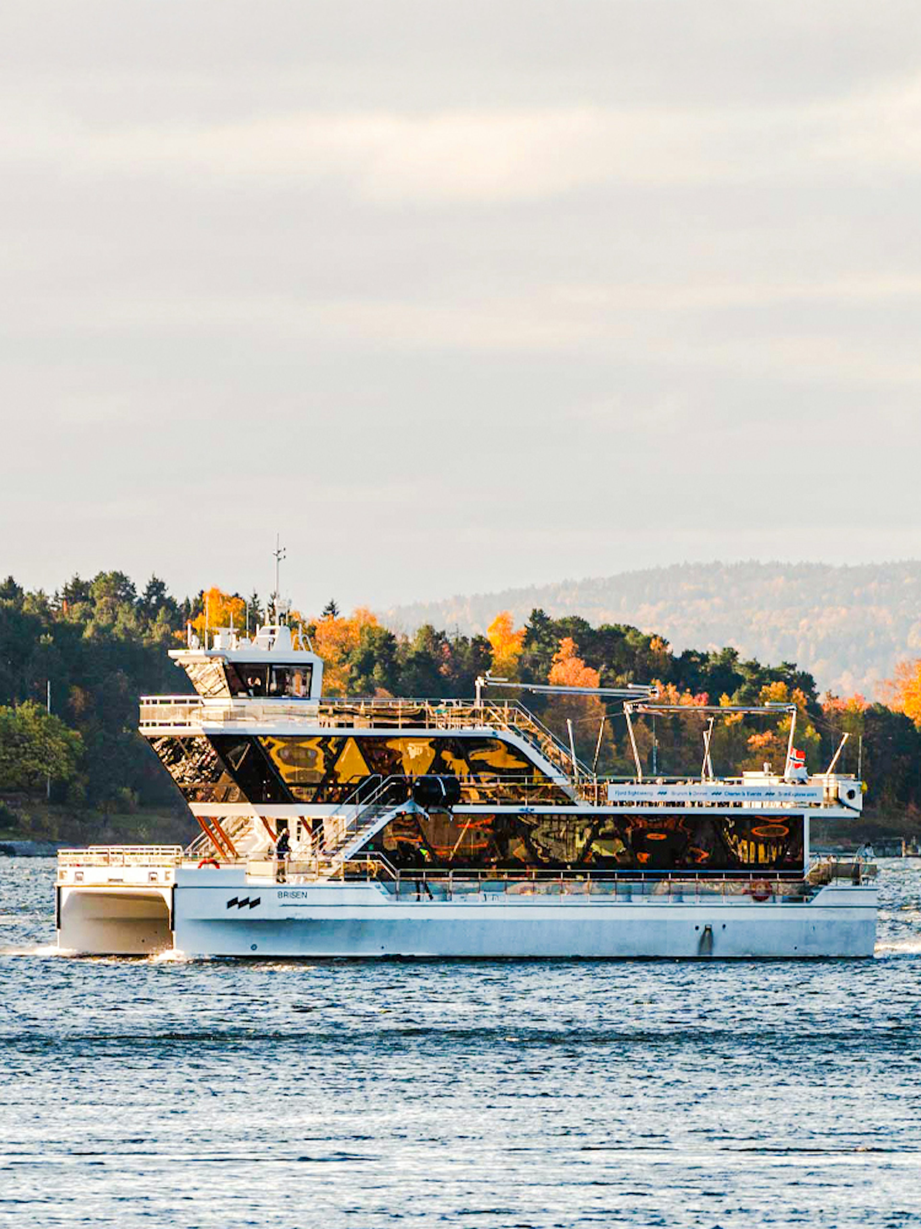 Silent fjord cruise boat on Oslofjord with autumn trees in the background.