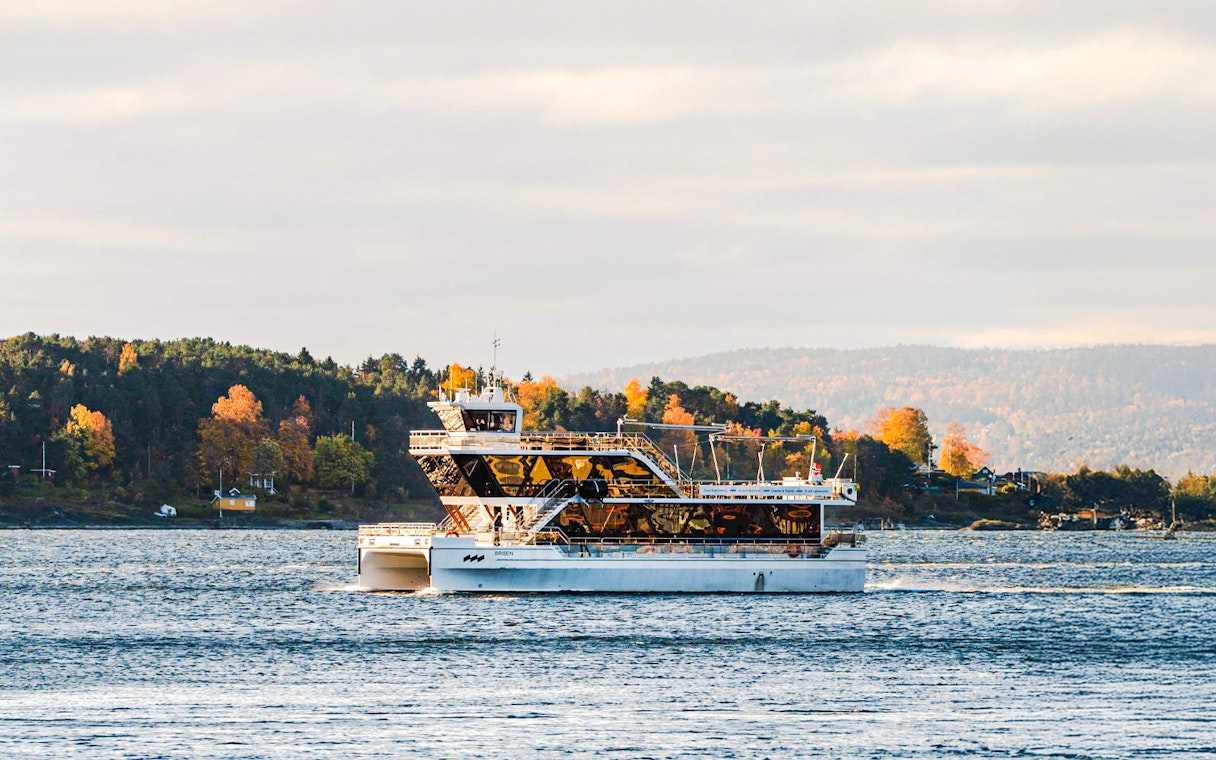 Silent fjord cruise boat on Oslofjord with autumn trees in the background.