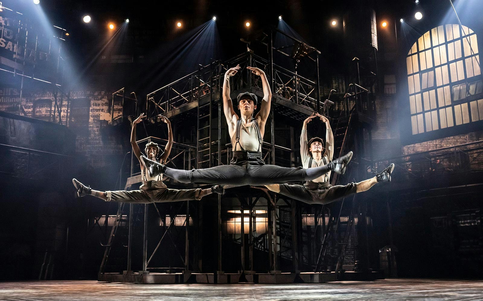 Performers in mid-air leap during Newsies stage show.