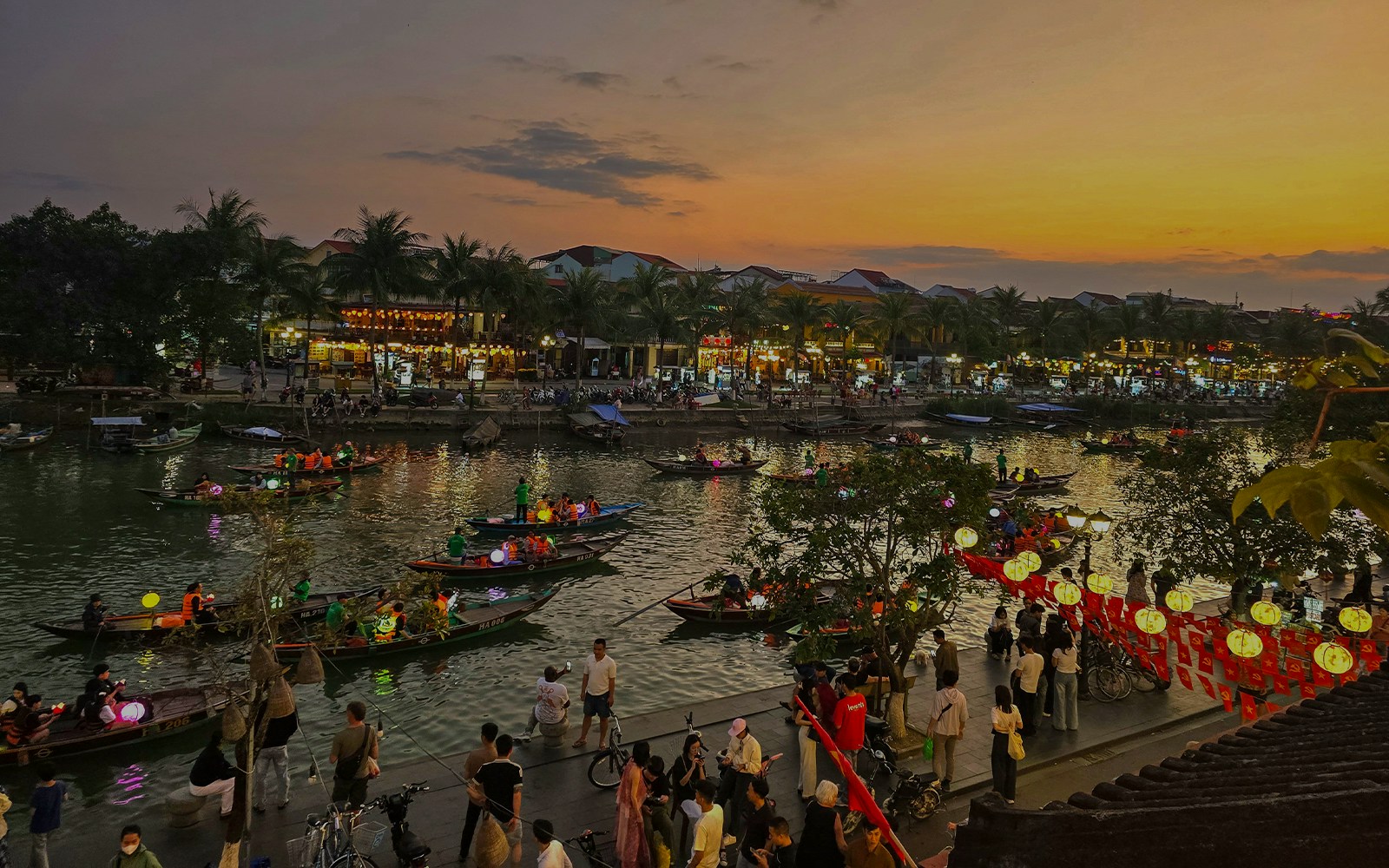 Hoi An river night market with lantern-lit boats and bustling riverside activity.