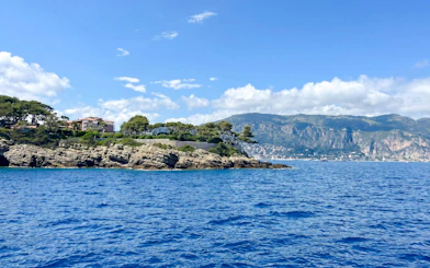 Coastal view from Villefranche boat tour to Monaco with rocky shoreline and distant mountains.
