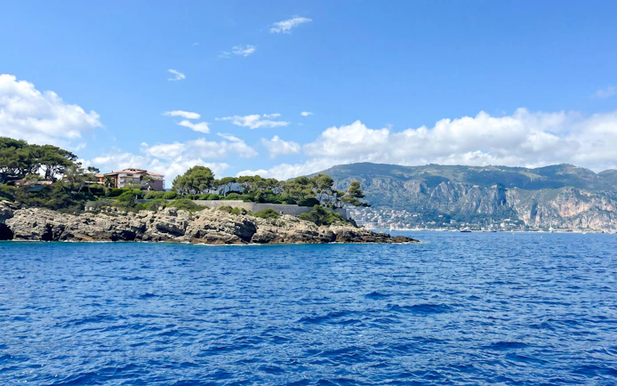 Coastal view from Villefranche boat tour to Monaco with rocky shoreline and distant mountains.
