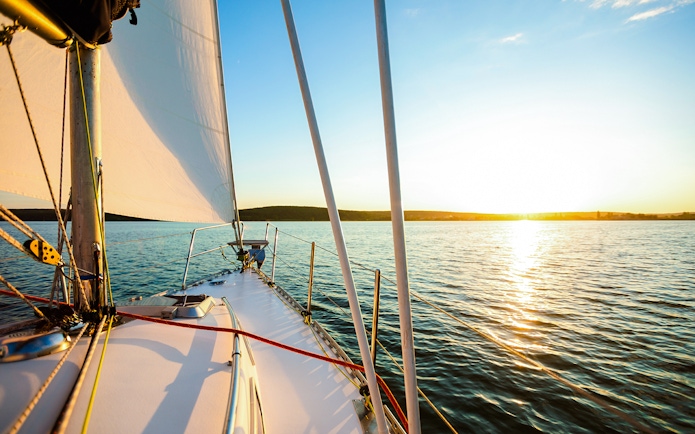White sailboat on Lisbon waters at sunset.