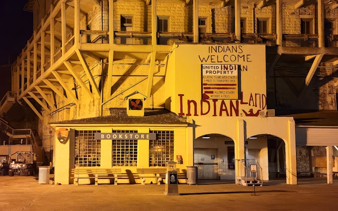 Alcatraz Island bookstore and historic "Indians Welcome" sign at night during ferry tour.