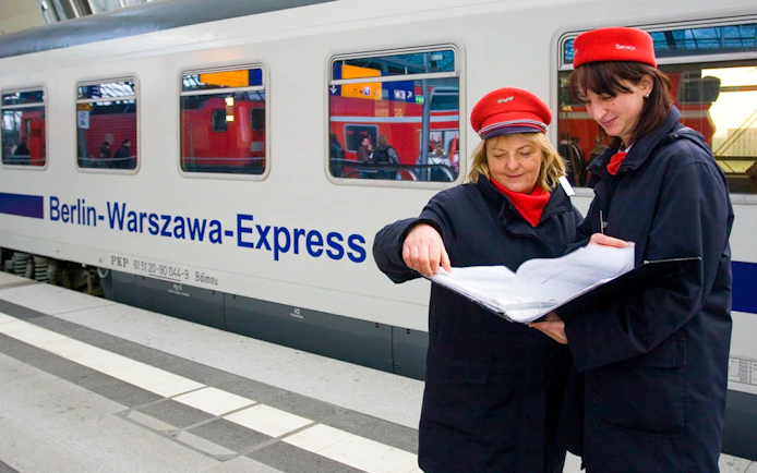 Train conductors reviewing documents beside Berlin-Warszawa-Express in Germany.