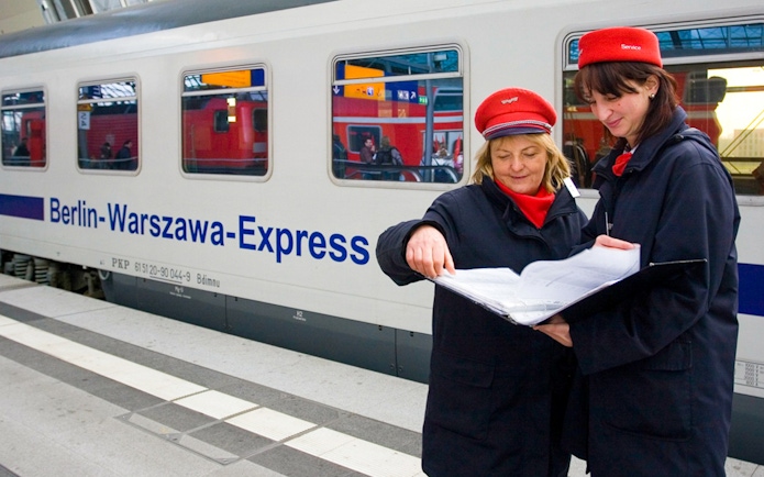 Train conductors reviewing documents beside Berlin-Warszawa-Express in Germany.