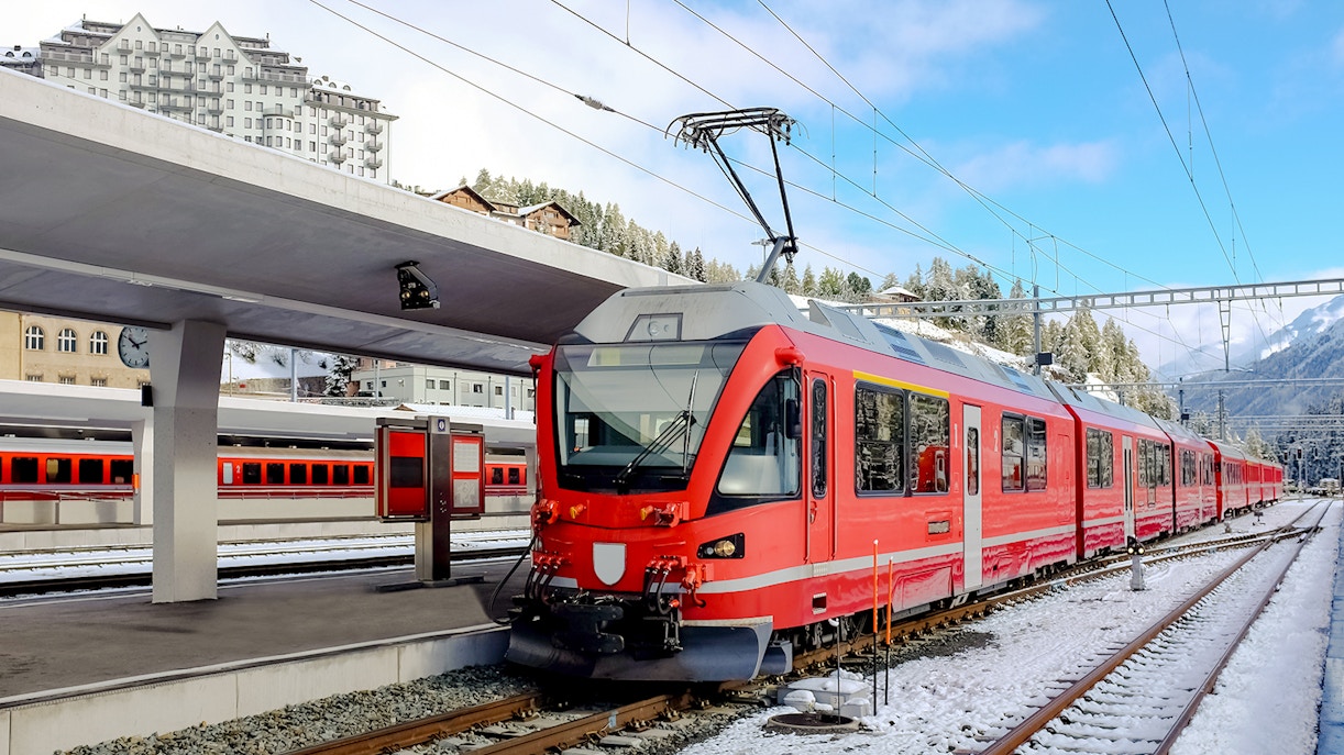 Red train at a snowy station in the Swiss Alps.