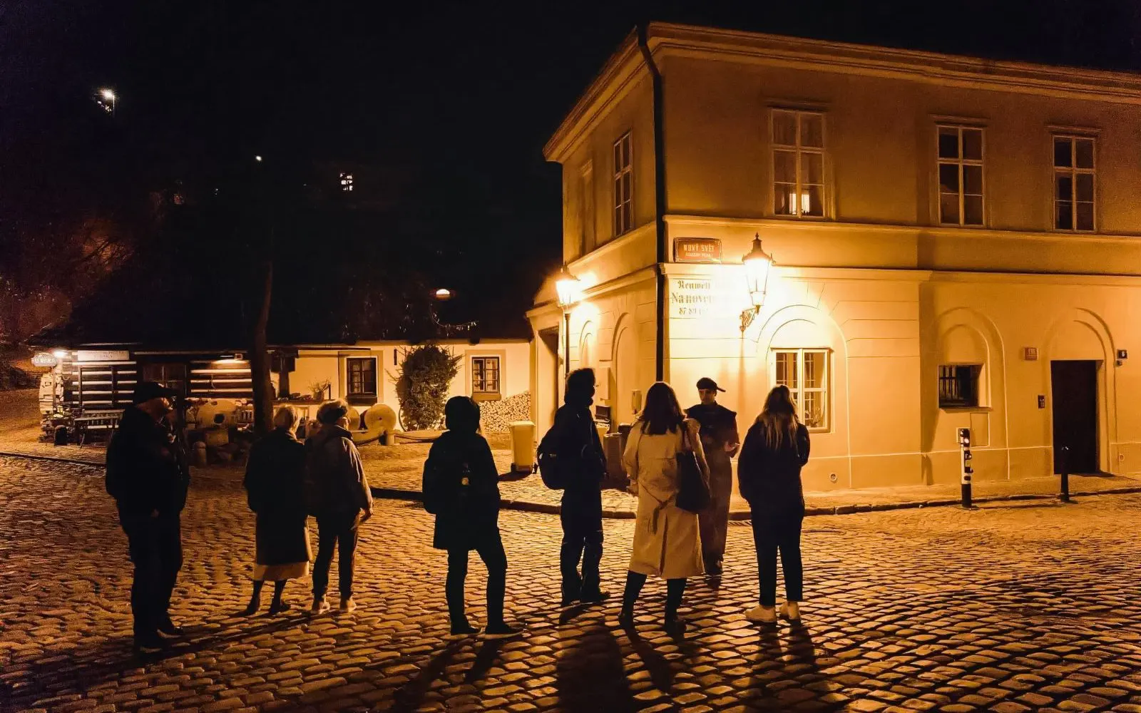 Group on a night tour outside Prague Castle, exploring historical streets.